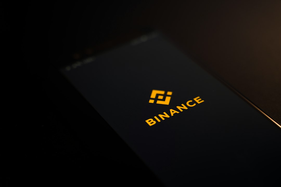 Ein Smartphone-Bildschirm zeigt das Binance-Logo und den Namen in gelber Farbe auf schwarzem Hintergrund und hebt damit Krypto-Innovationen in der modernen Geschäftswelt hervor.