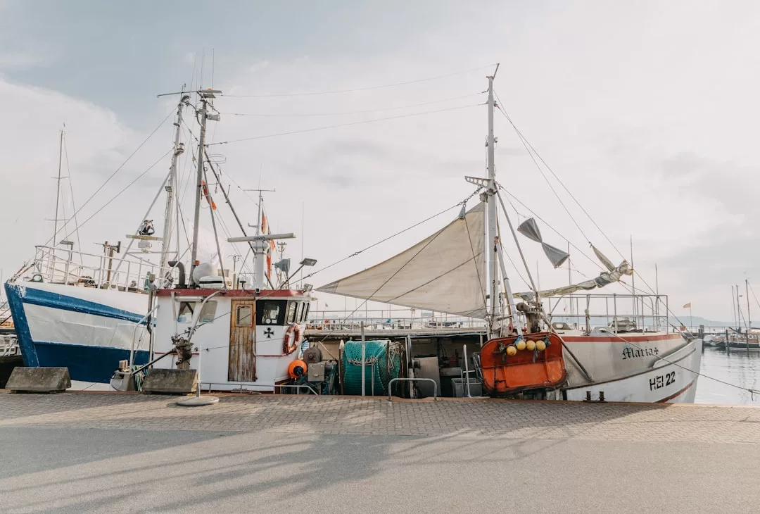 Zwei Fischerboote liegen in einem Hafen vor Anker, mit verschiedenen Netzen an Deck. Der bewölkte Himmel und andere Boote im Hintergrund machen deutlich, warum Häfen wie dieser zu den besten Sehenswürdigkeiten Kiels für Besucher gehören.