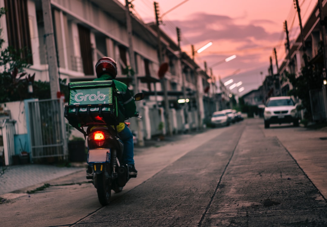 Ein Lieferfahrer mit Helm fährt bei Sonnenuntergang auf einem Motorrad mit einer Grabbeltasche durch eine Wohnstraße und verkörpert damit den rasanten Geist der Gig Economy.